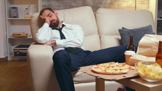 Overworked businessman sleeping on the couch. Fast food on the table.