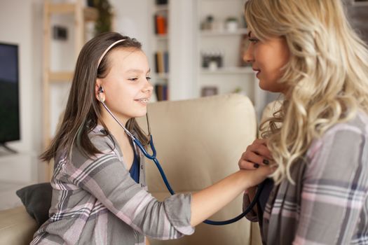 Female doctor teaching her little girl how to use stethoscope to listen her heart.