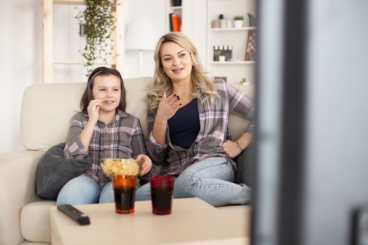 Young mother and her little girl resting on sofa watching tv.