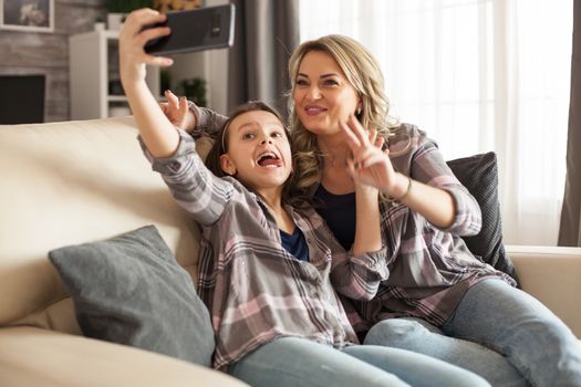 Funny little daughter and her mother are taking a selfie using smartphone. Happy kid.