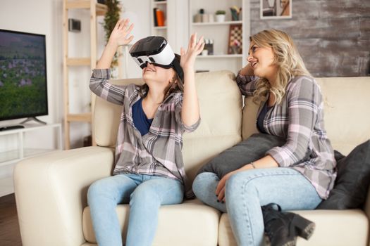 Amazed little girl sitting next to her mother on the couch while using virtual reality headset.