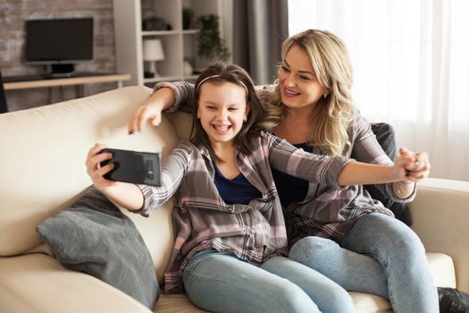 Little girl with braces and her mother taking a selfie sitting on the couch in living room.