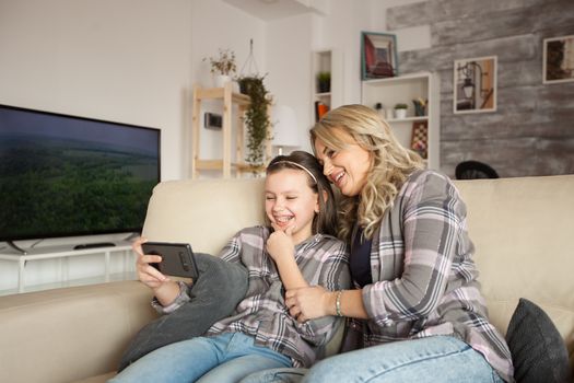 Happy child and her mother watching a funny video on smartphone.