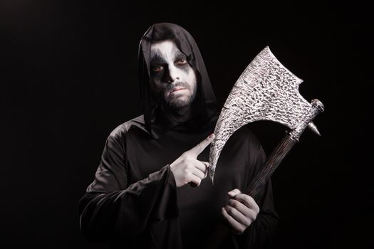 Dangerous scary man dressed up like grim reaper with an axe over black background.