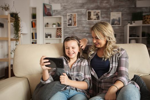 Little girl with braces smiling while using phone app. Mother spending time with her daughter.