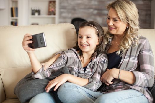Mother and daughter relaxing together watching a video on smartphone sitting on the couch.