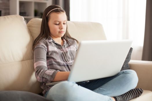 Little girl with long hair sitting on the couch in living room using laptop.