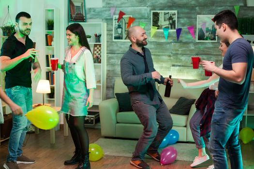 Group of cheerful young people dancing at party with good music and balloons.