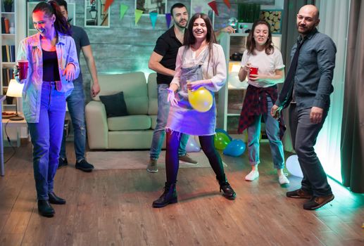 Young woman laughing because of balloon helium while dancing at the party with her friends.