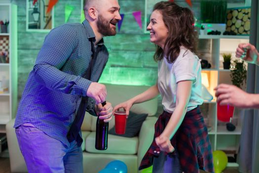 Cheerful young man and woman at a party dancing. Man holding a beer bottle.