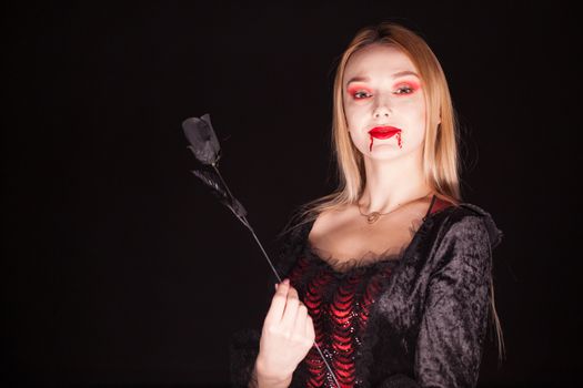 Caucasian vampire woman with bloody lips over black background. Halloween costume.