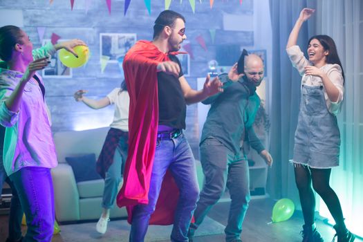 Group of friends enjoying their time at a party in a room with neon lights. Man in superhero costume.