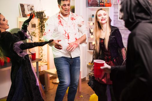 Man dressed up like a creepy zombie dancing at halloween celebration with his friends.