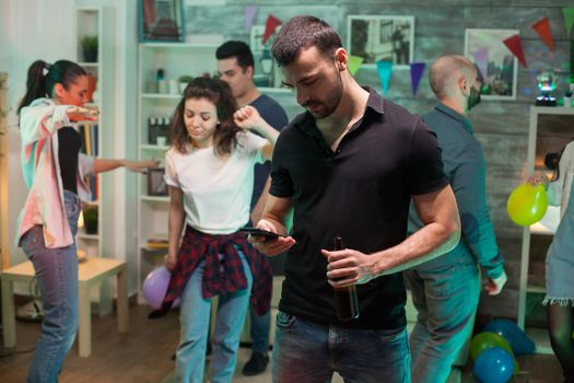 Young man browsing on his mobile phone at a party with disco music.