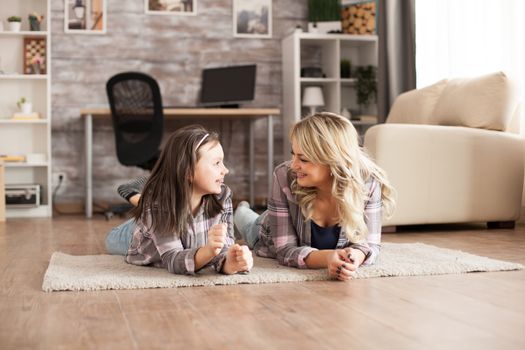 Cheerful young mother and her teenage daughter lying on the carpet in living room.