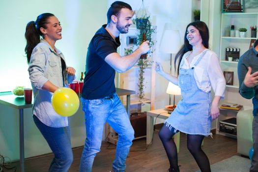 Young woman holding a balloon while dancing with her friends at a party. Man with a beer bottle.