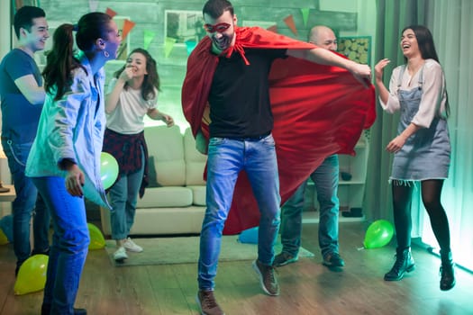 Caucasian man wearing superhero costume jumping in the air at friends party.
