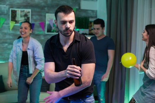 Cheerful male holding a beer bottle while dancing with his friends at party in his home.