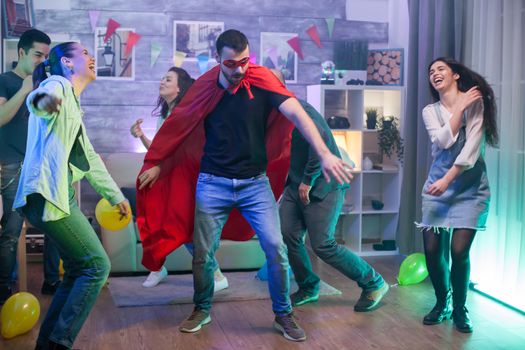 Young man in superhero costume dancing in centre of the room., Group of people dancing.