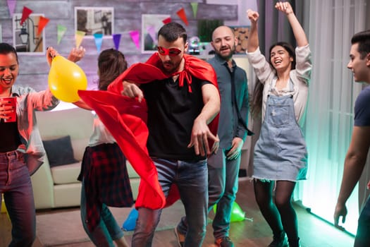 Handsome man in superhero costume dancing on disco music at friends party.