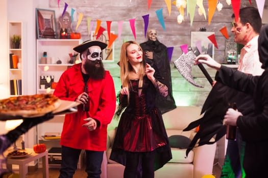 Young woman dressed up like a witch for halloween arriving with pizza at the party.