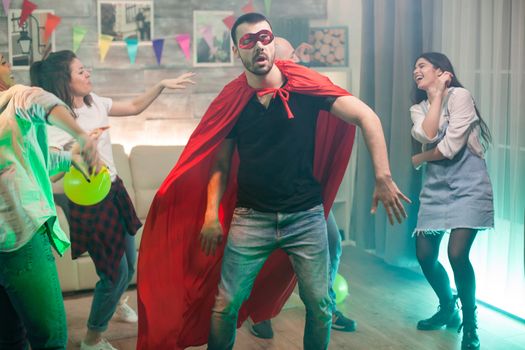 Handsome man in red superhero costume partying with his friends. Joyful woman.