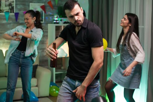 Attractive young man with a beer bottle in his hand dancing at a party with friends. Girl with balloon.