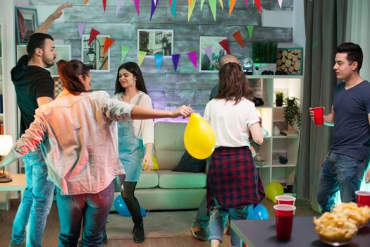 Joyful young woman holding a balloon while dancing with her friends at a party.