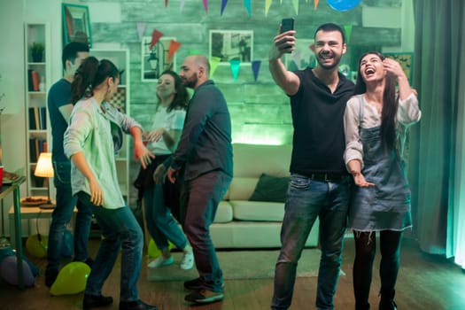 Young man laughing while taking a selfie with beautiful woman while having fun at the party.