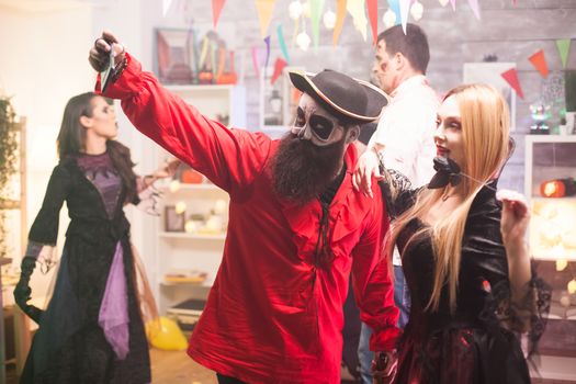 Attractive man and woman dressed up like pirate and vampire taking a selfie at halloween party.