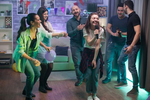 Happy woman singing for her friends at the party. Karaoke entertainment.