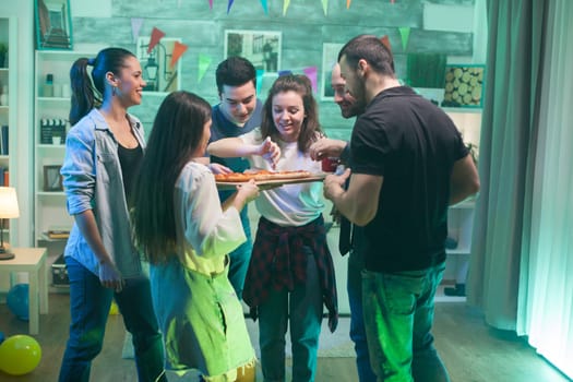 Young woman taking the big sliece of pizza at the party. Group of cheerful young people.