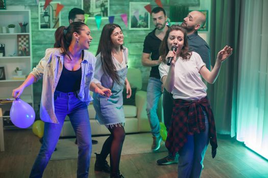 Beautiful young woman holding the microphone while doing karaoke with her friends.