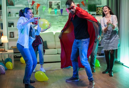 Beautiful young woman holding a balloon at a party and looking at her friend dressed up like a super hero.