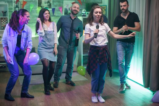 Young beautiful woman surrounded by her friends doing karaoke at the party.