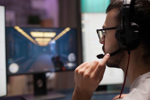 Competitive young man playing shooter video games wearing headphones in a room with neon light.