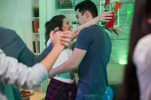 Beautiful young woman with arms around her boyfriend neck dancing at a party.