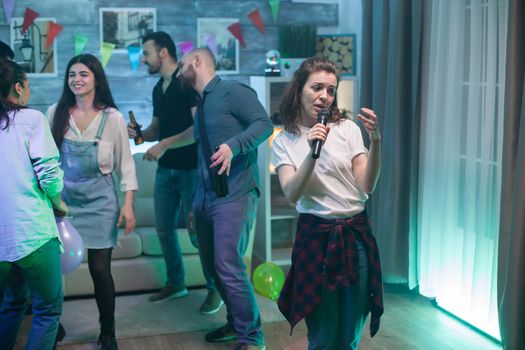 Beautiful young woman in a white t-shirt doing karaoke at a party with group of friends.