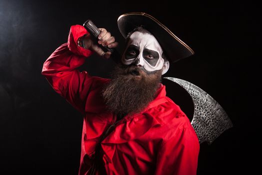 Crazy man dressed up like a medieval pirate with long beard and his axe for halloween over black background.