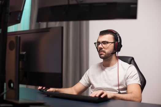 Portrait of professional gamer playing shooter games on powerful computer with multiple monitors.