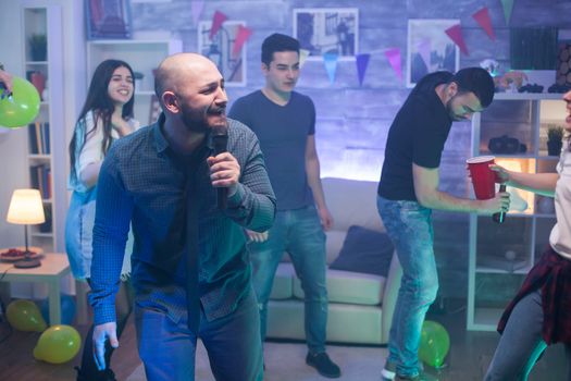 Young caucasian man singing on microphone for his friends entertainment at the party.