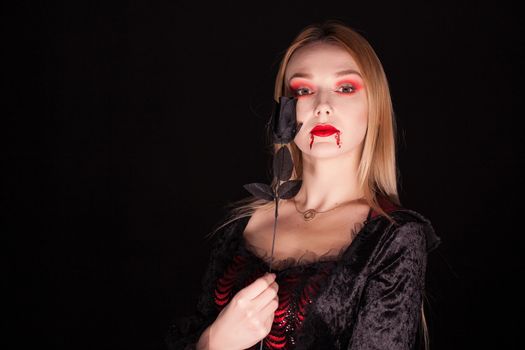 Beautiful blond vampire woman with a rose over black background for halloween.