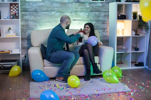 Attractive bald man and beautiful woman having a conversation sitting on the couch at a party. Having a drink.