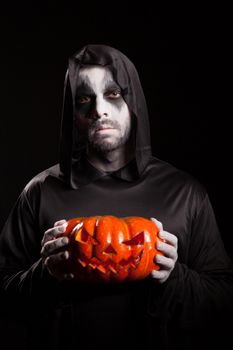 Spooky grim reaper holding a pumpkin over black background, Halloween outfit.