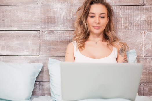 Pretty blonde woman working late at night on her laptop wearing pajamas .