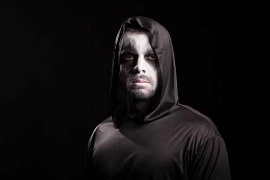 Young man looking serious into the camera dressed up like grim reaper. Halloween costume.