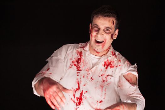 Cheerful man dressed up like a scary zombie over black background. Halloween creative makeup.