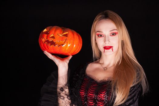 Portrait of beautiful girl dressed up like a vampire holding a pumpkin for halloween.