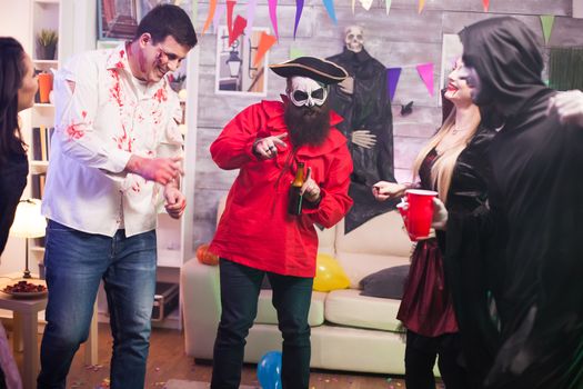 Man with pirate costume holding a beer at halloween celebration with his friends.