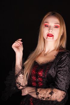 Vampire beautiful woman with bloody lips over black background. Halloween costume.